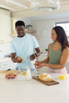 African American couple wearing casual clothes cracking eggs into mixing bowl at kitchen island