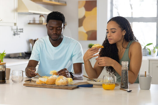 African American couple sitting at counter using cutting board with rolls, French press visible