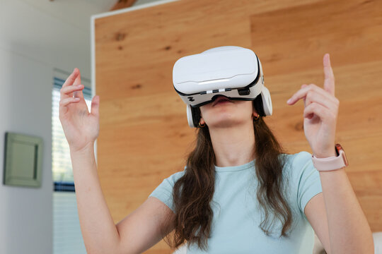 Woman wearing white VR headset raising hands, showing pink wrist wearable at home