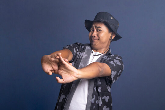 Young man wearing a black bucket hat and patterned shirt stretching his arms forward with interlocking fingers while making a tired or reluctant facial expression.