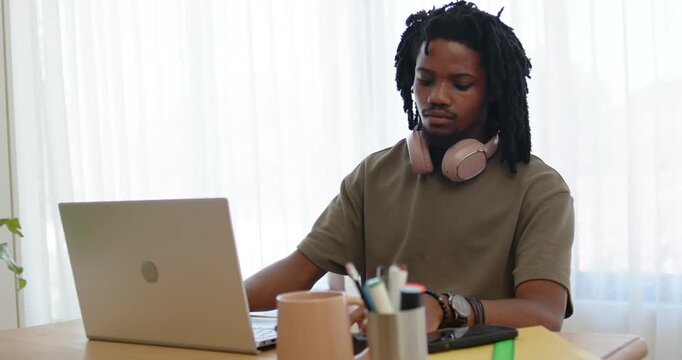 Man sitting at desk, gazing between laptop and smartphone, reaching to interact while working