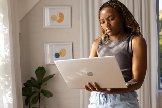 African American woman wearing gray tank holding silver laptop with circular logo at home