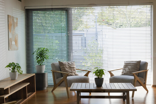 Pair of wooden-framed armchairs facing wooden coffee table near window with blinds, showing plants