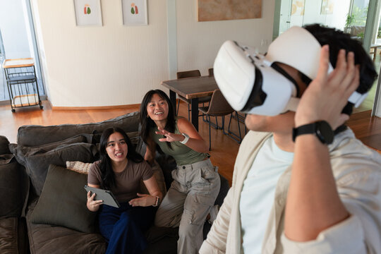 Diverse friends interacting in living room with man adjusting white VR headset, tablet, copy space