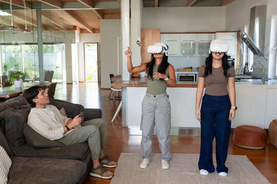 Diverse friends standing near kitchen island in open-plan living area wearing white VR headsets