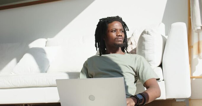 African American male gazing at sunlight then shifting to silver laptop on white sofa, working