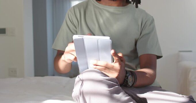 African man on bed propping folio tablet on knee, adjusting grip and tapping for steady viewing