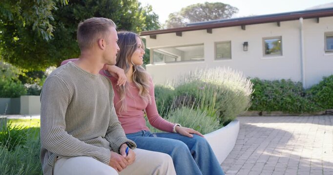 Diverse couple sitting on curved bench in front yard, spotting right, pointing blue remote, leaning
