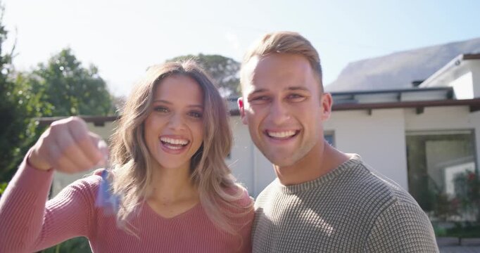 Couple waving blue keychain outside modern house, woman turning from door, celebrating purchase