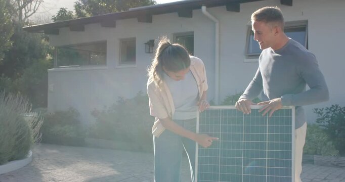 Diverse couple inspecting PV at house, woman starting pointing at cells, man pointing roof planning