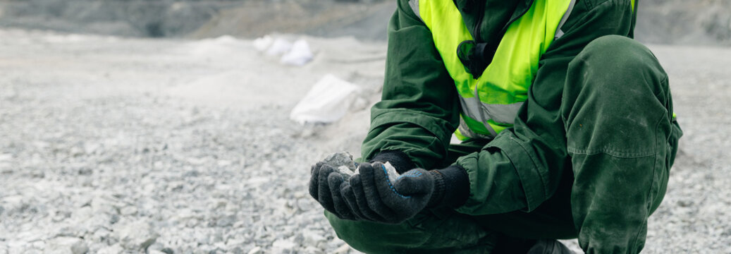 Worker examining rock sample in open gravel quarry site.