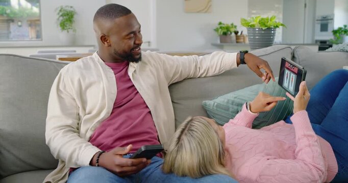 Couple on light-gray sofa, man holding phone, pointing at tablet while woman tapping to share plans