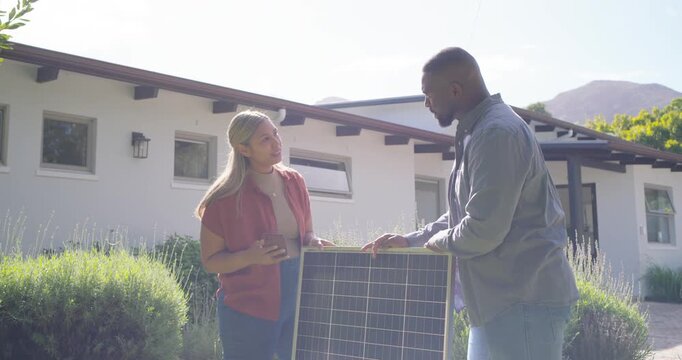 Homeowner showing smartphone and contractor inspecting solar panel in front yard and reviewing plan