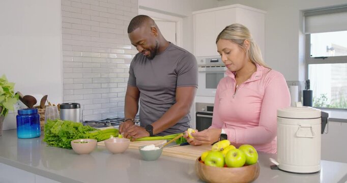Couple prepping meal at kitchen island man chopping greens on wood boards as woman peeling banana