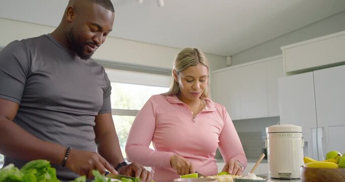 African American couple in kitchen prepping meal, chopping greens, slicing fruit, composting scraps