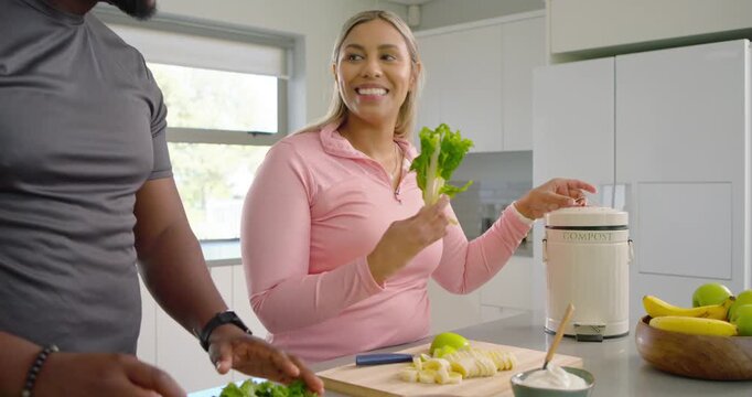 African American couple making salad at island chopping greens, slicing fruit, using compost bin