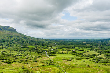 Obraz premium Patchwork green fields and hedgerows spread across the countryside near Gleniff in County Sligo, Ireland. A peaceful rural landscape beneath heavy clouds.