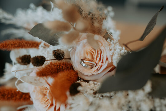 Composition florale de mariage aux tons p&ecirc;che et terracotta avec alliances en premier plan 