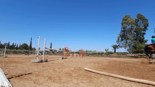 Close-up of a bay horse and rider jumping over a fence in an outdoor equestrian arena. The rider, dressed in black athletic gear and a helmet, 