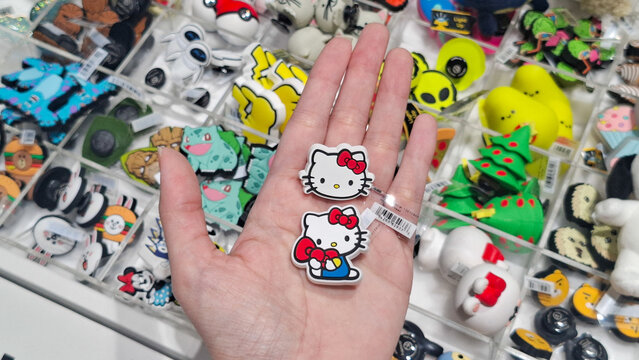 Hand holding Hello Kitty rubber character charms for Crocs clog shoes at a Sanrio merchandise retail display on May 9, 2026 in Bangkok, Thailand 