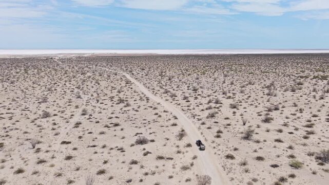 Aerial view shows SUV pulling teardrop camper trailer in Baja desert near El Salar salt flats in Baja California under blue sky.