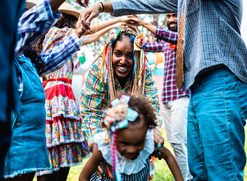 Happy Afro-Brazilian family celebrating Festa Junina with traditional dance and colorful costumes in a backyard.
