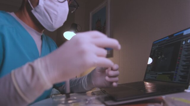 Male laboratory technician with a face mask and gloves examining a blood sample tube at his desk