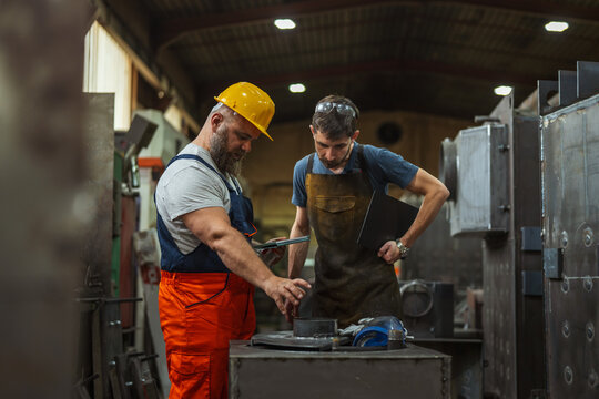 Metalworkers discussing manufacturing process in industrial factory