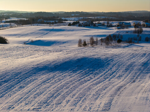Aerial view of snow-covered rolling hills and rural houses under a soft golden sunset light Lithuania.