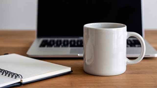Minimalist home office desk setup featuring a white ceramic coffee mug open notebook with spiral binding and a sleek laptop on a warm wooden surface evoking focus and productivity