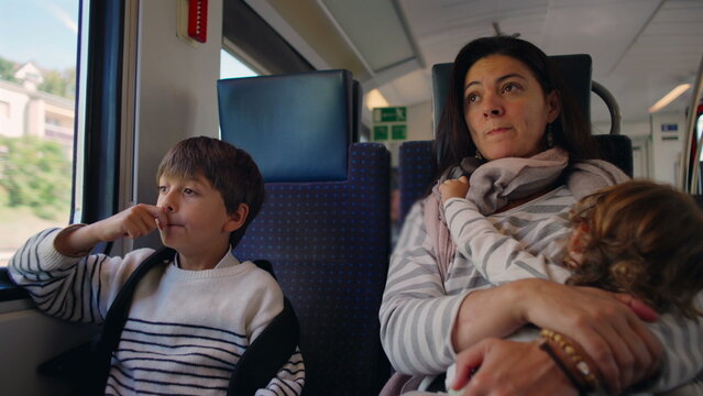 Child sitting beside mother on train while she breastfeeds toddler creating real moment of family connection travel fatigue and everyday closeness during moving journey