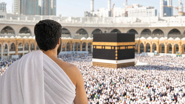 Muslim pilgrim man wearing white ihram clothes looking at the holy Kaaba in the Great Mosque of Mecca during Hajj or Umrah pilgrimage in Saudi Arabia for religious concepts.