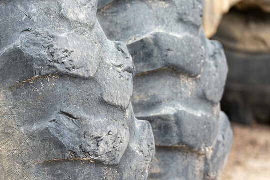 Close-up of heavy tractor tire tread, covered in dust and grime. Deep grooves show wear from rugged terrain. Ideal for agriculture, construction, or industrial themes. Suggests strength, durability
