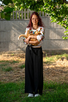 Young woman holding cat in embroidered blouse outdoors