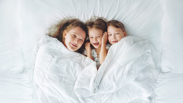 Happy family - portrait of children and mother in bed. Happy, love and fun at home. Family, childhood.