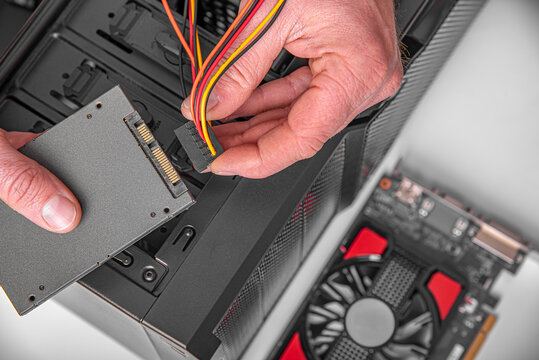 A technician connects a power cable to a solid state drive during a desktop computer assembly.