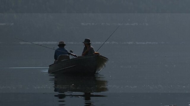 Two men approaching camera in boat, current nudging craft, adjusting rods, fishing with reflections