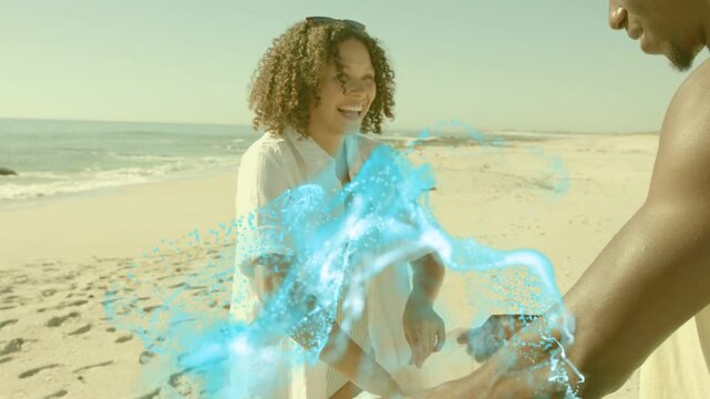 Woman opening bag on beach as man passing item, causing blue wave around hands for marketing