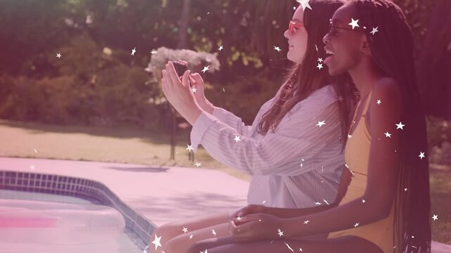 Two teen girls poolside raising phone to frame selfie for marketing, sparkles drifting over faces
