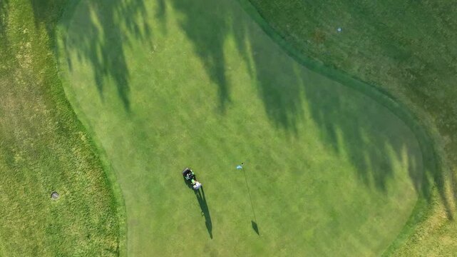 Aerial view of a golfer putting on the green with cart and flagstick visible