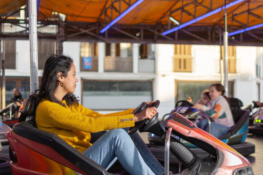 young Hispanic woman driving bumper car at village carnival