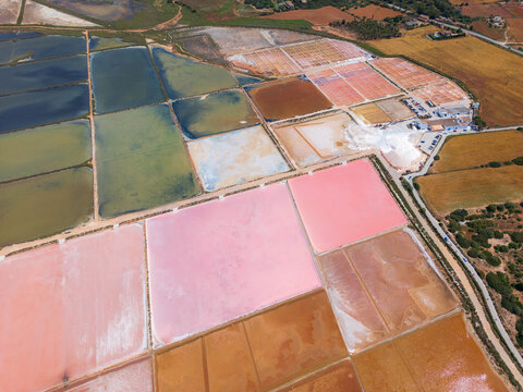 Aerial view of the colorful salt evaporation ponds at Salines des Trenc with vibrant pink and orange water under bright daylight in Campos, Islas Baleares, Spain.