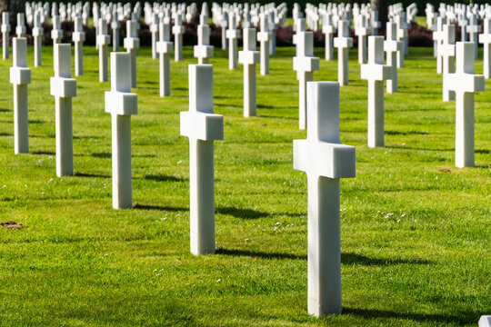 American cemetery in Normandy with rows of military grave markers on green lawn. World War II remembrance and national tribute
