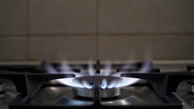 Close up of blue gas flame burning on a kitchen stove top with tiled background