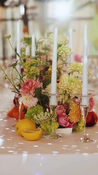 Vertical video of premium wedding aesthetic. Minimalist floral design with citrus accents and white candles on a banquet table with no people and no food. High-end visual for brand storytelling