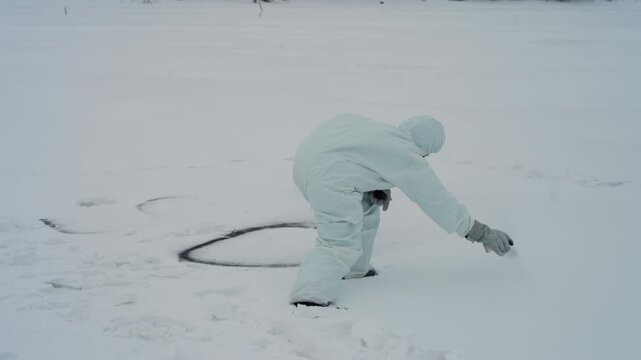 White suited technician draws dark circle on snowy ice marking recovery perimeter, bending to scrape snow away, scattered footprints, tense rescue atmosphere, overcast winter light