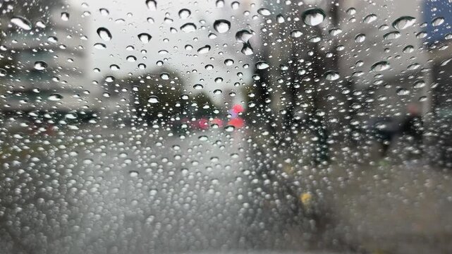 close view of a soft rain drops on a windshield with a blurred traffic bakground