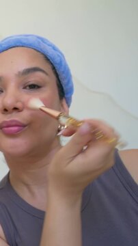 Vertical video: Opening pink box blue-plush-headband demo host dipping brush applying blush at home