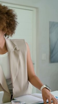 Vertical video: Writing after look, curly woman in blazer sorting notebook at island for planning