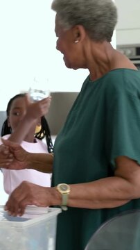 Vertical video: Reaching bins, gran teaching girl to sort glass jars into GLASS or PLASTIC in kitche